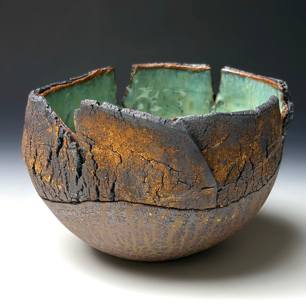A handmade ceramic bowl with a textured, cracked exterior in dark brown and gold tones, and a glossy light green glazed interior, shown on a neutral gradient background.