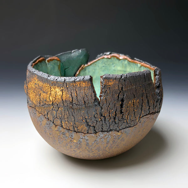 A handmade ceramic bowl with a unique cracked, broken-edge exterior and a glossy green glazed interior, photographed on a dark-to-light gradient studio background.