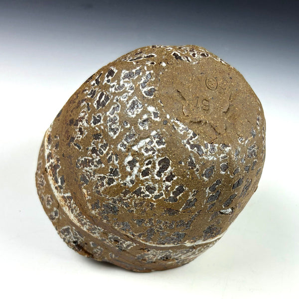 A textured ceramic object with a speckled brown and white glaze, photographed on a white surface with a gray gradient background.