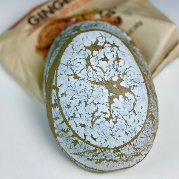 A close-up of a gingerbread cookie with a white powdered sugar dusting and browned edges, with a gingerbread bag partially visible in the background.